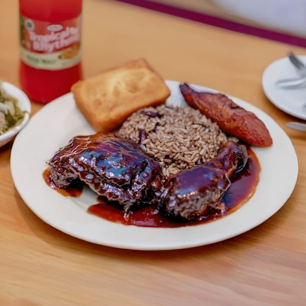 Soul food plate with dark glazed chicken, rice and beans, cornbread, and plantain.