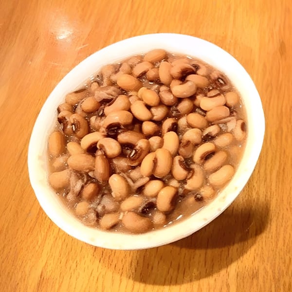 A white bowl filled with black-eyed peas and broth, served on a wooden table.