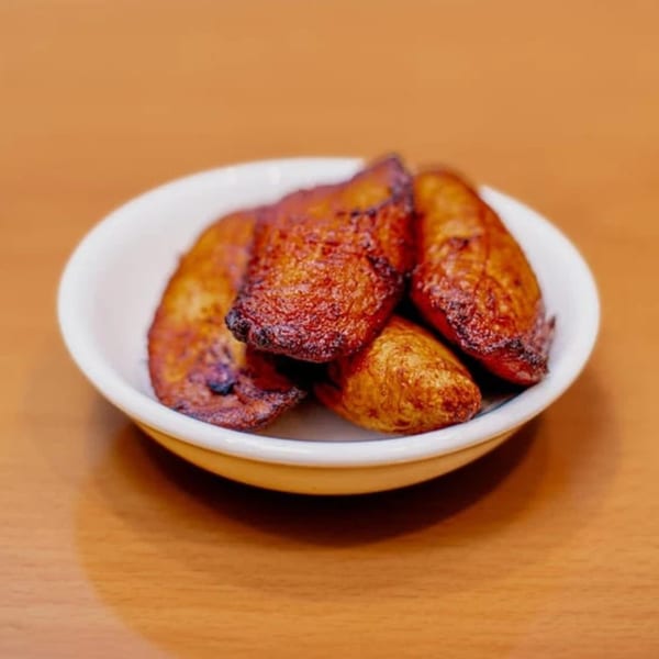 A small white bowl filled with several pieces of golden-brown fried plantains on a wooden table.