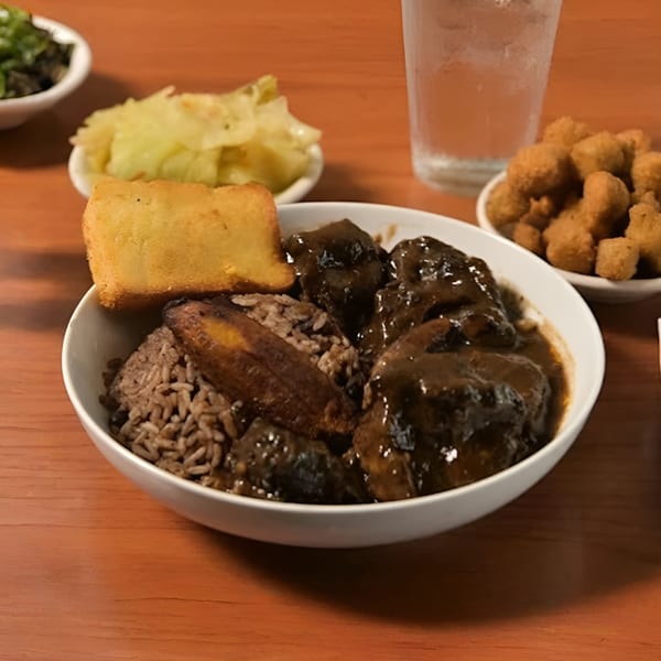 A bowl of Jake's Soulfood Cafe's oxtails and rice, with cornbread, cabbage, and fried okra.